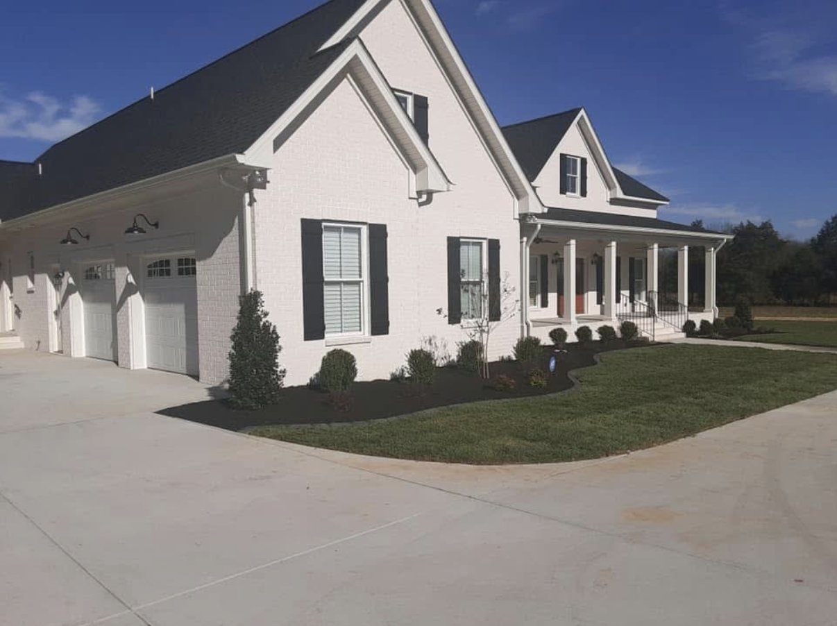 Curved mulched planting bed along driveway at white farmhouse-style home