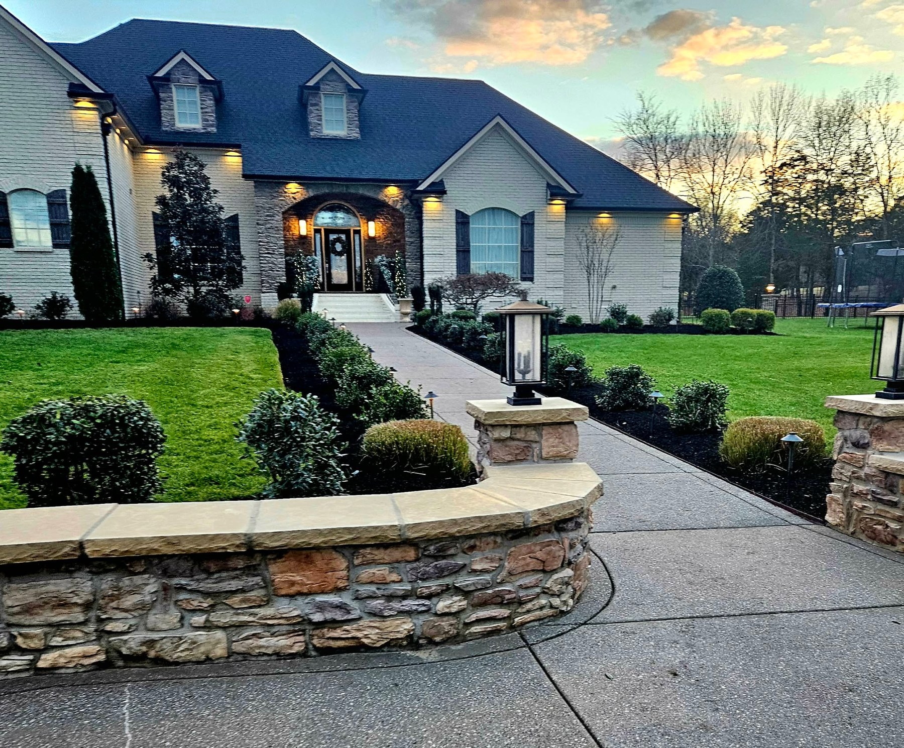 Jordan's Landscaping front yard with stone wall, walkway, and landscape lighting at dusk